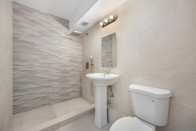 bathroom with toilet, visible vents, a tile shower, and tile walls