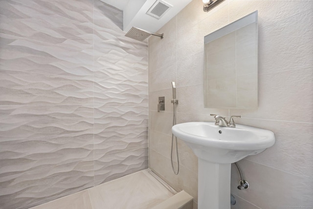 bathroom with a sink, tile walls, visible vents, and tiled shower