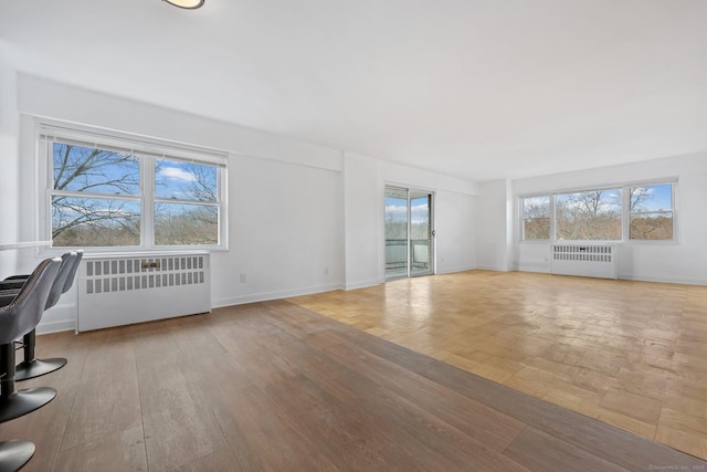 unfurnished living room with radiator heating unit, wood finished floors, and baseboards