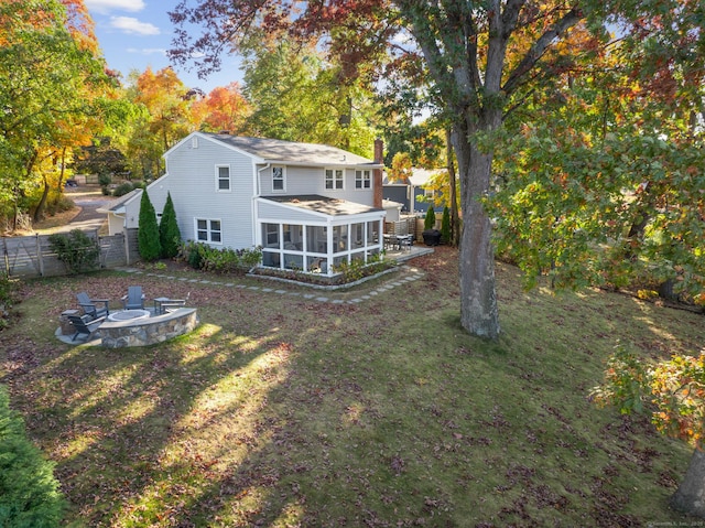 back of house featuring a fire pit, a sunroom, a fenced backyard, a chimney, and a yard