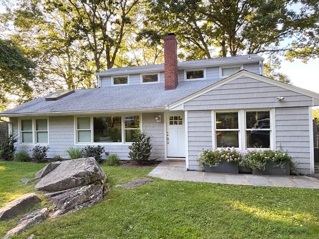 traditional-style house with roof with shingles, a chimney, and a front yard