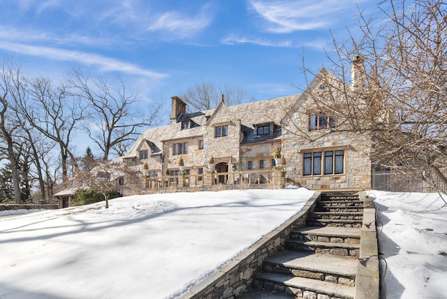 snow covered back of property featuring stone siding and a chimney