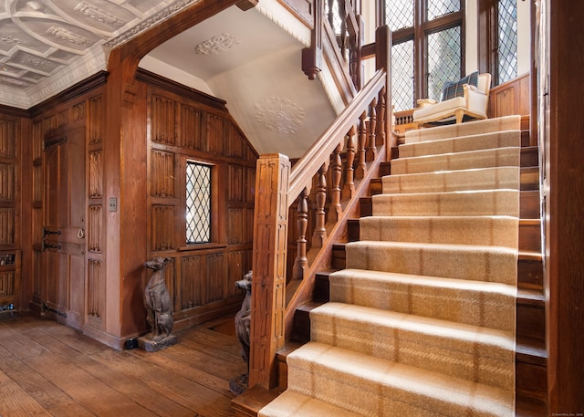 staircase with lofted ceiling, plenty of natural light, wooden walls, and hardwood / wood-style flooring