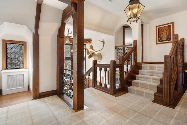 foyer with arched walkways, light colored carpet, baseboards, vaulted ceiling, and radiator