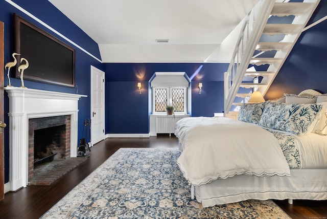 bedroom with a brick fireplace, visible vents, baseboards, and wood finished floors