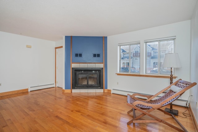 sitting room with visible vents, baseboard heating, a tile fireplace, and light wood-style flooring