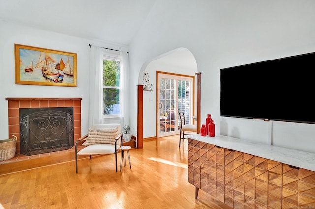 living area with baseboards, arched walkways, a tiled fireplace, lofted ceiling, and wood finished floors