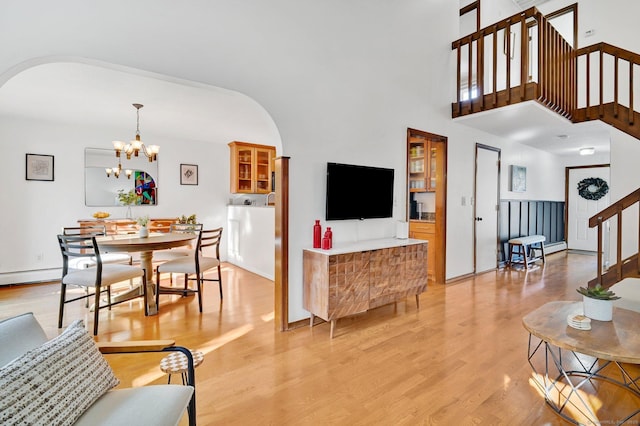 living room featuring arched walkways, a chandelier, light wood-style flooring, a towering ceiling, and stairway