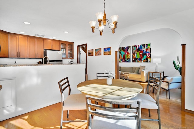 dining space featuring arched walkways, light wood-type flooring, an inviting chandelier, and recessed lighting