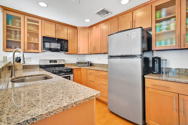 kitchen featuring light stone counters, stainless steel appliances, a sink, visible vents, and glass insert cabinets