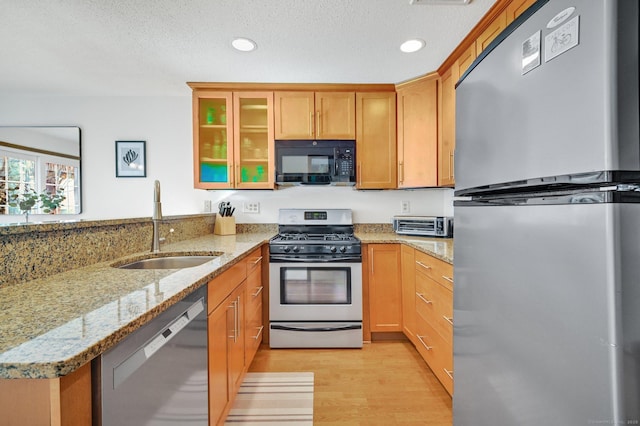 kitchen with light wood finished floors, glass insert cabinets, light stone counters, stainless steel appliances, and a sink