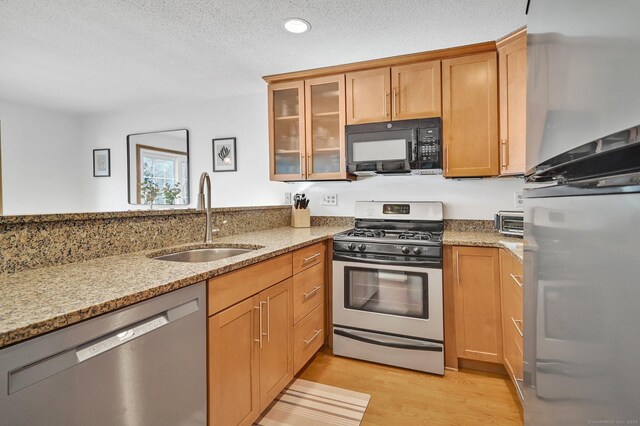 kitchen with light wood finished floors, glass insert cabinets, appliances with stainless steel finishes, light stone counters, and a sink