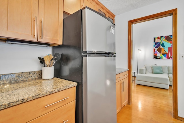 kitchen featuring light stone countertops, light wood-style flooring, a textured ceiling, and freestanding refrigerator