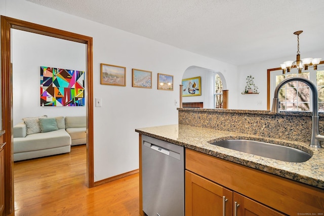 kitchen with light wood finished floors, hanging light fixtures, light stone countertops, stainless steel dishwasher, and a sink