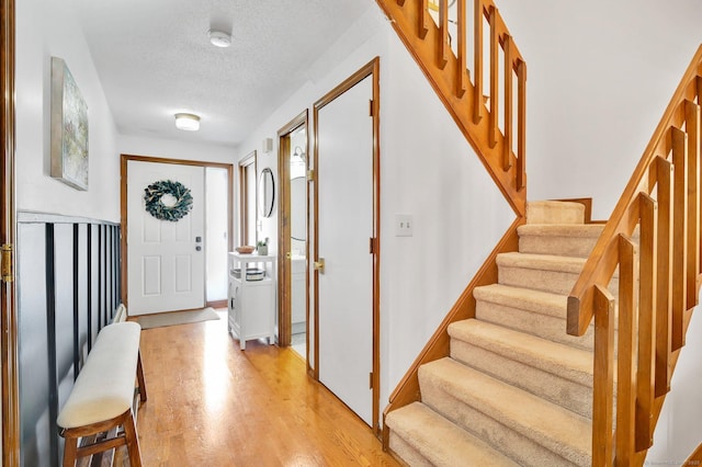 foyer entrance with stairway, baseboards, light wood-style flooring, and a textured ceiling