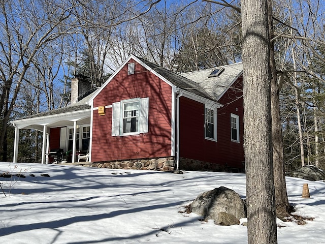 view of snow covered exterior with covered porch, roof with shingles, and a chimney