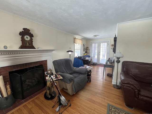 living area featuring a textured ceiling, a fireplace, french doors, light wood finished floors, and crown molding