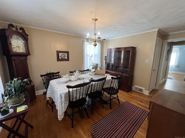 dining space with light wood-type flooring, an inviting chandelier, visible vents, and crown molding