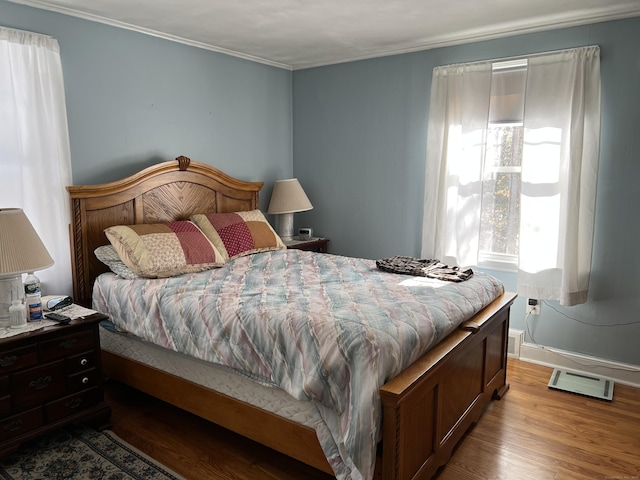 bedroom featuring baseboards, visible vents, ornamental molding, and wood finished floors