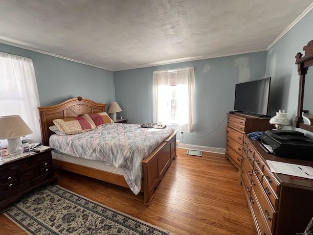 bedroom featuring light wood finished floors, baseboards, and crown molding