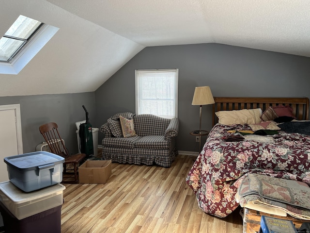 bedroom featuring a textured ceiling, lofted ceiling with skylight, baseboards, and light wood-style floors