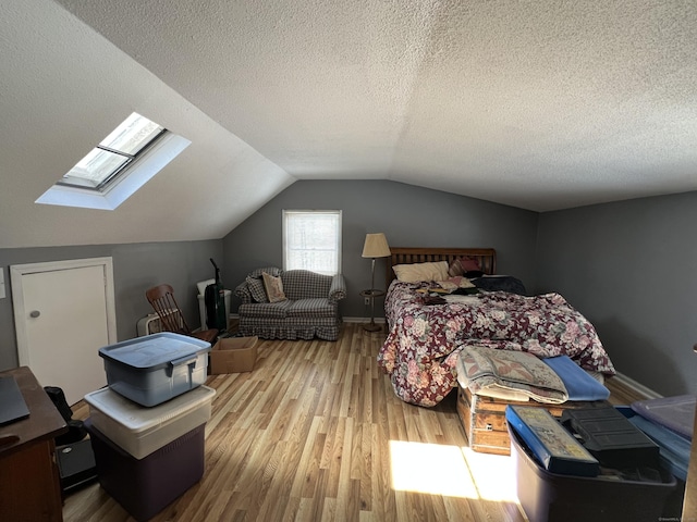 bedroom featuring a textured ceiling, vaulted ceiling with skylight, wood finished floors, and baseboards