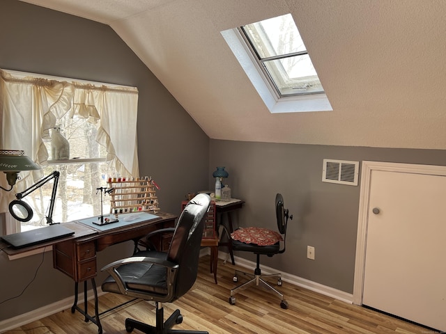 office space featuring vaulted ceiling with skylight, visible vents, baseboards, and wood finished floors