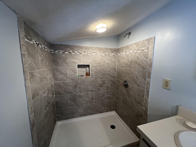 bathroom featuring a textured ceiling, a tile shower, and vanity