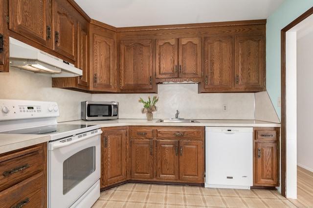 kitchen with under cabinet range hood, white appliances, light countertops, and a sink