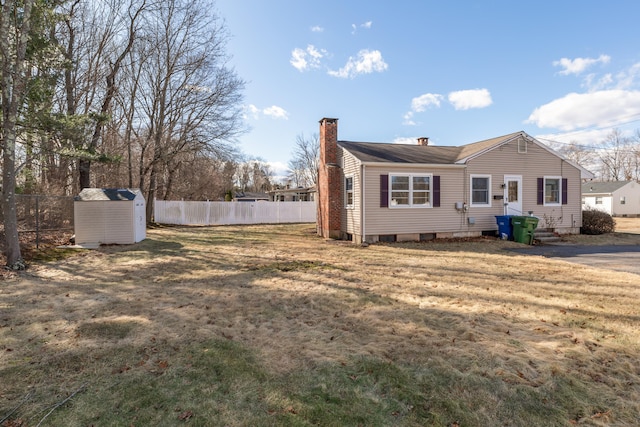 exterior space with fence, a shed, a lawn, a chimney, and an outbuilding