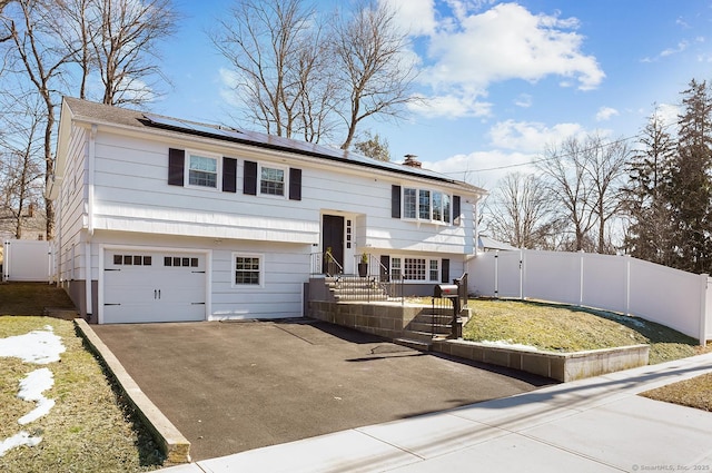 raised ranch with aphalt driveway, an attached garage, a gate, fence, and roof mounted solar panels