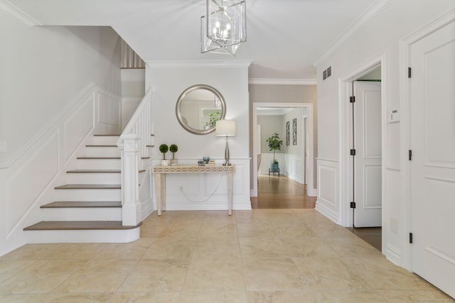 tiled foyer entrance with a chandelier, a decorative wall, visible vents, stairs, and ornamental molding