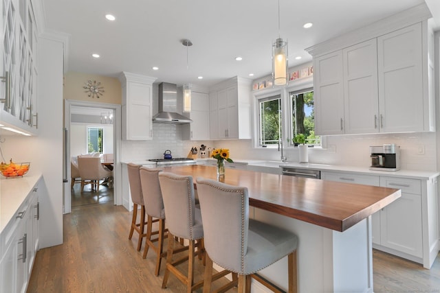 kitchen featuring a breakfast bar area, white cabinetry, wood counters, wood finished floors, and wall chimney exhaust hood