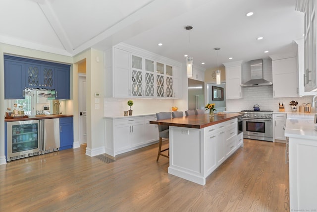 kitchen with butcher block counters, wine cooler, high end range, a center island, and wall chimney range hood