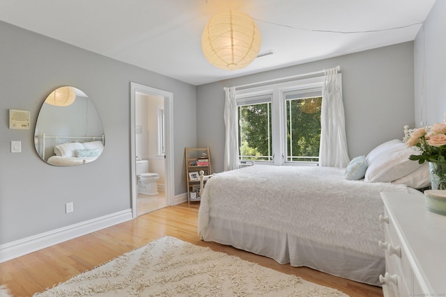 bedroom with ensuite bath, wood finished floors, visible vents, and baseboards