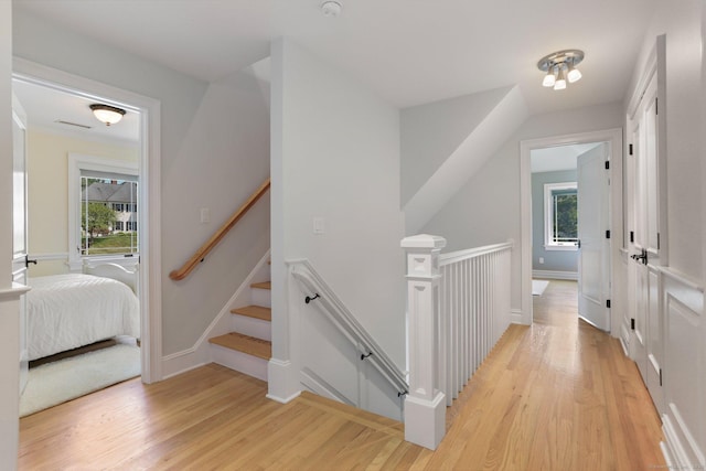 hallway with light wood-style flooring, baseboards, and an upstairs landing