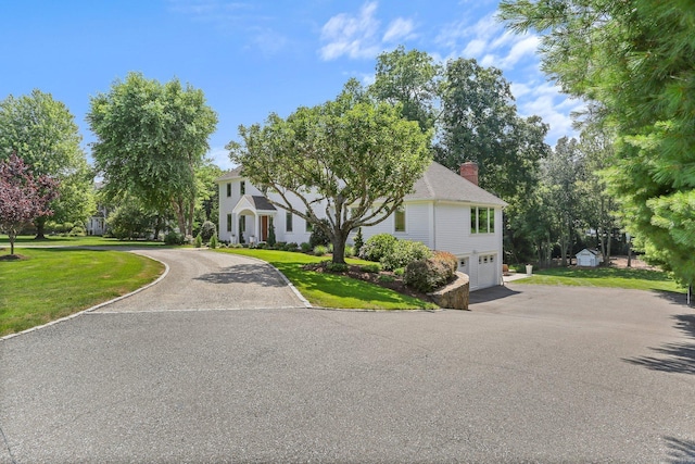 view of front of property with a garage, a front lawn, curved driveway, and a chimney