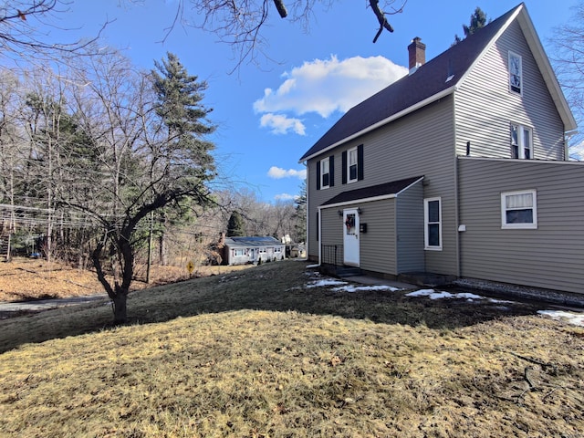 view of side of home with entry steps, a lawn, and a chimney