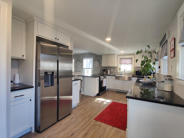 kitchen with white cabinets, appliances with stainless steel finishes, a peninsula, light wood-type flooring, and a sink