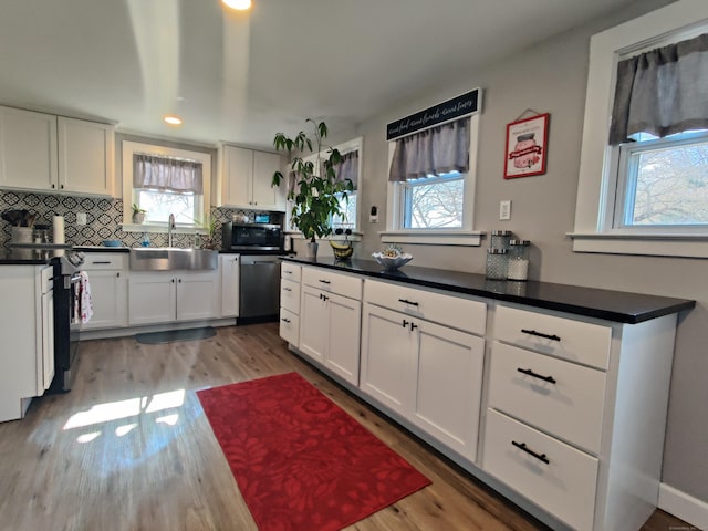 kitchen featuring tasteful backsplash, appliances with stainless steel finishes, white cabinetry, a sink, and light wood-type flooring