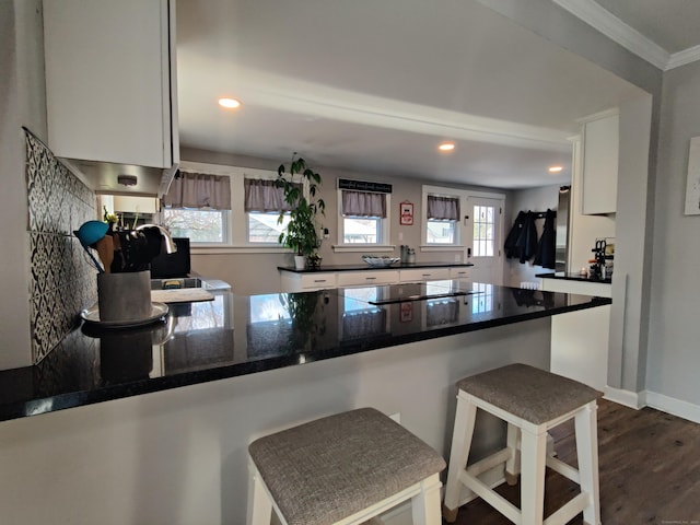 kitchen with dark wood-style floors, a breakfast bar area, black electric stovetop, white cabinetry, and a peninsula