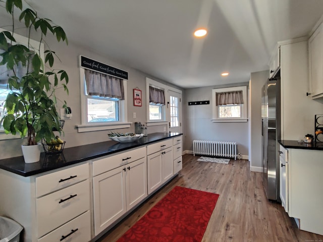 kitchen with baseboards, radiator, wood finished floors, freestanding refrigerator, and white cabinetry