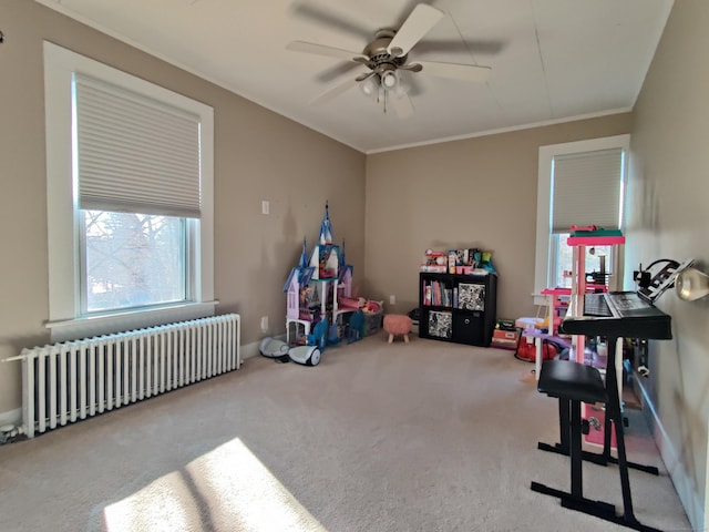 playroom featuring baseboards, radiator, ceiling fan, ornamental molding, and carpet floors