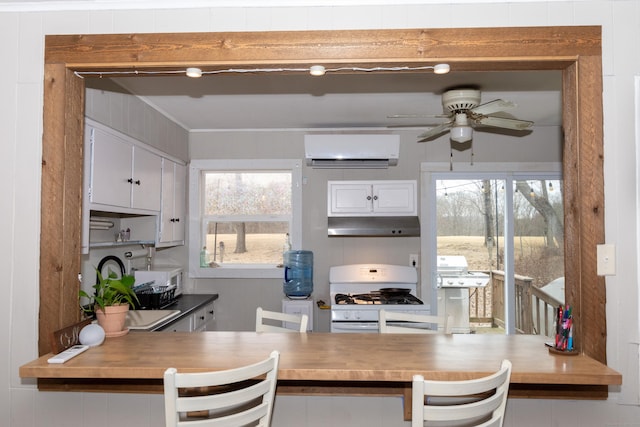 kitchen with a ceiling fan, a wall mounted air conditioner, under cabinet range hood, white cabinetry, and gas range gas stove