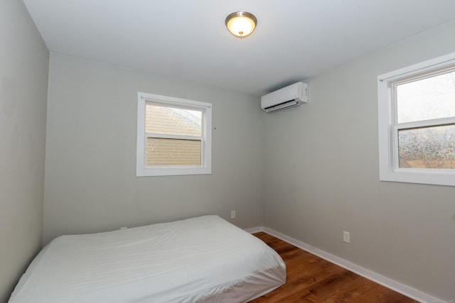 bedroom featuring multiple windows, a wall mounted AC, wood finished floors, and baseboards