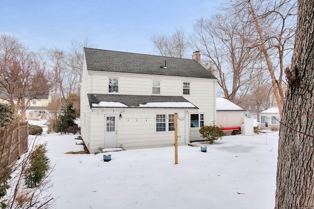 snow covered back of property featuring a shingled roof, a chimney, and fence