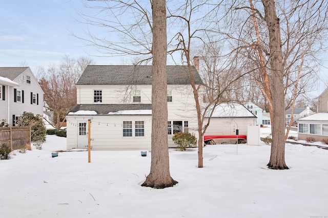 snow covered back of property featuring roof with shingles and fence