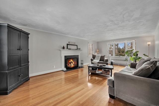 living room with radiator, light wood-style flooring, ornamental molding, a warm lit fireplace, and baseboards