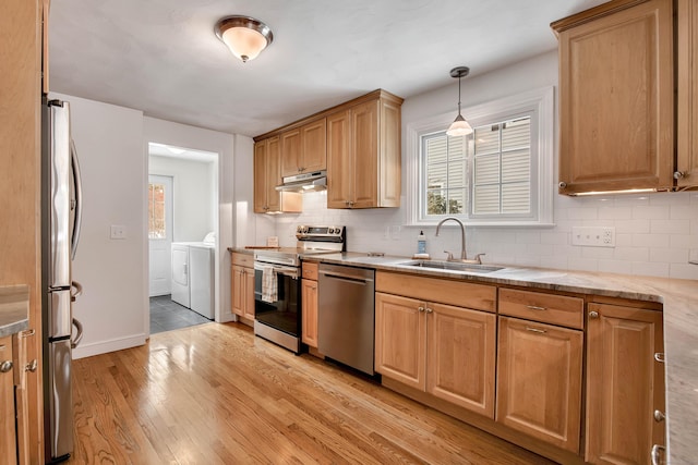 kitchen with light wood finished floors, stainless steel appliances, a sink, independent washer and dryer, and under cabinet range hood