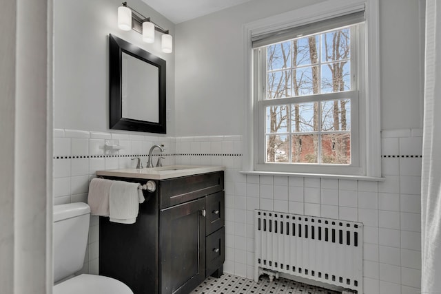 bathroom with toilet, a wainscoted wall, vanity, tile walls, and radiator